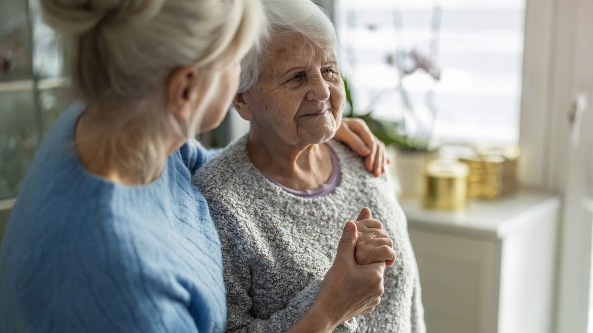 Bundesregierung will Pflege-Trick für Rentner ab 2027 beenden 1 Zwei ältere Frauen sitzen zusammen in einer hellen Wohnung und halten sich an den Händen.