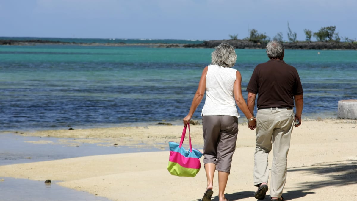 Älteres Paar geht Hand in Hand an einem Strand entlang.