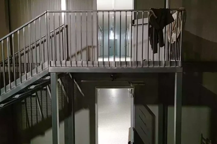 Treppenhaus in einem nüchternen Gebäude mit Metallgeländer und offenen Türen.
