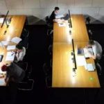 Studierende arbeiten an langen Tischen in einer Lern- oder Bibliotheksumgebung.