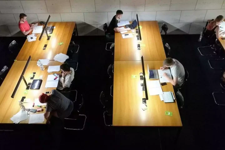 Studierende arbeiten an langen Tischen in einer Lern- oder Bibliotheksumgebung.