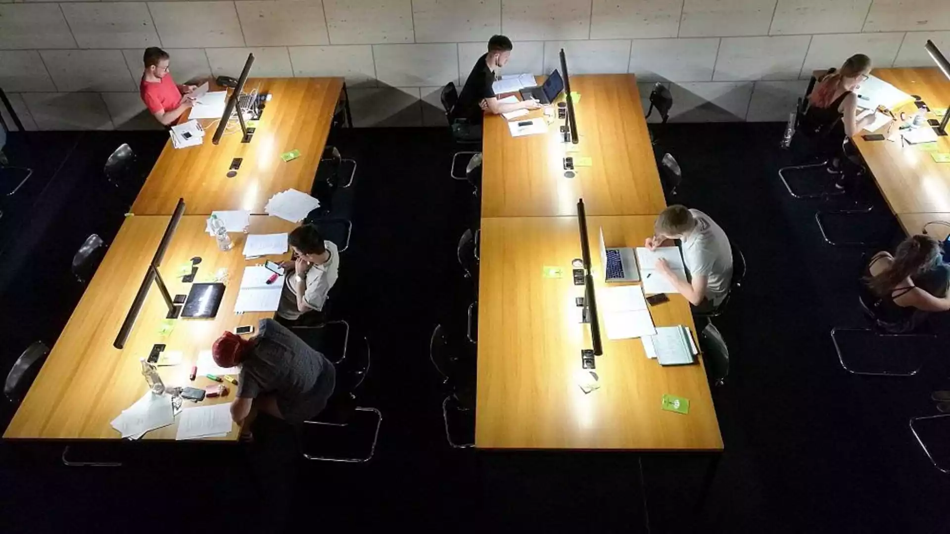 Studierende arbeiten an langen Tischen in einer Lern- oder Bibliotheksumgebung.