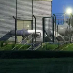 Blick auf eine Industrieanlage mit Rohrleitungen hinter einem Zaun.