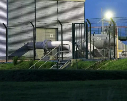 Blick auf eine Industrieanlage mit Rohrleitungen hinter einem Zaun.