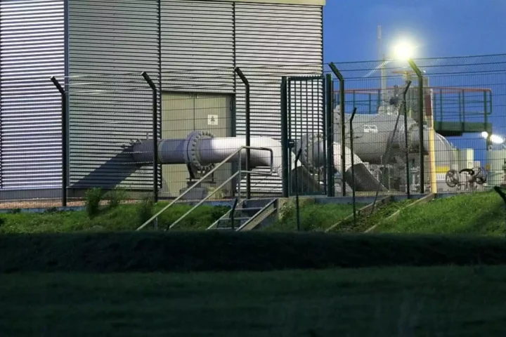 Blick auf eine Industrieanlage mit Rohrleitungen hinter einem Zaun.