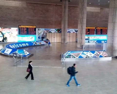 Innenhalle eines Flughafens mit Anzeigetafeln, Begrüßungsbeschilderung und wenigen Passanten.