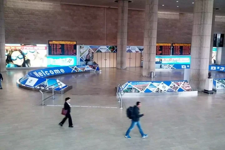 Innenhalle eines Flughafens mit Anzeigetafeln, Begrüßungsbeschilderung und wenigen Passanten.