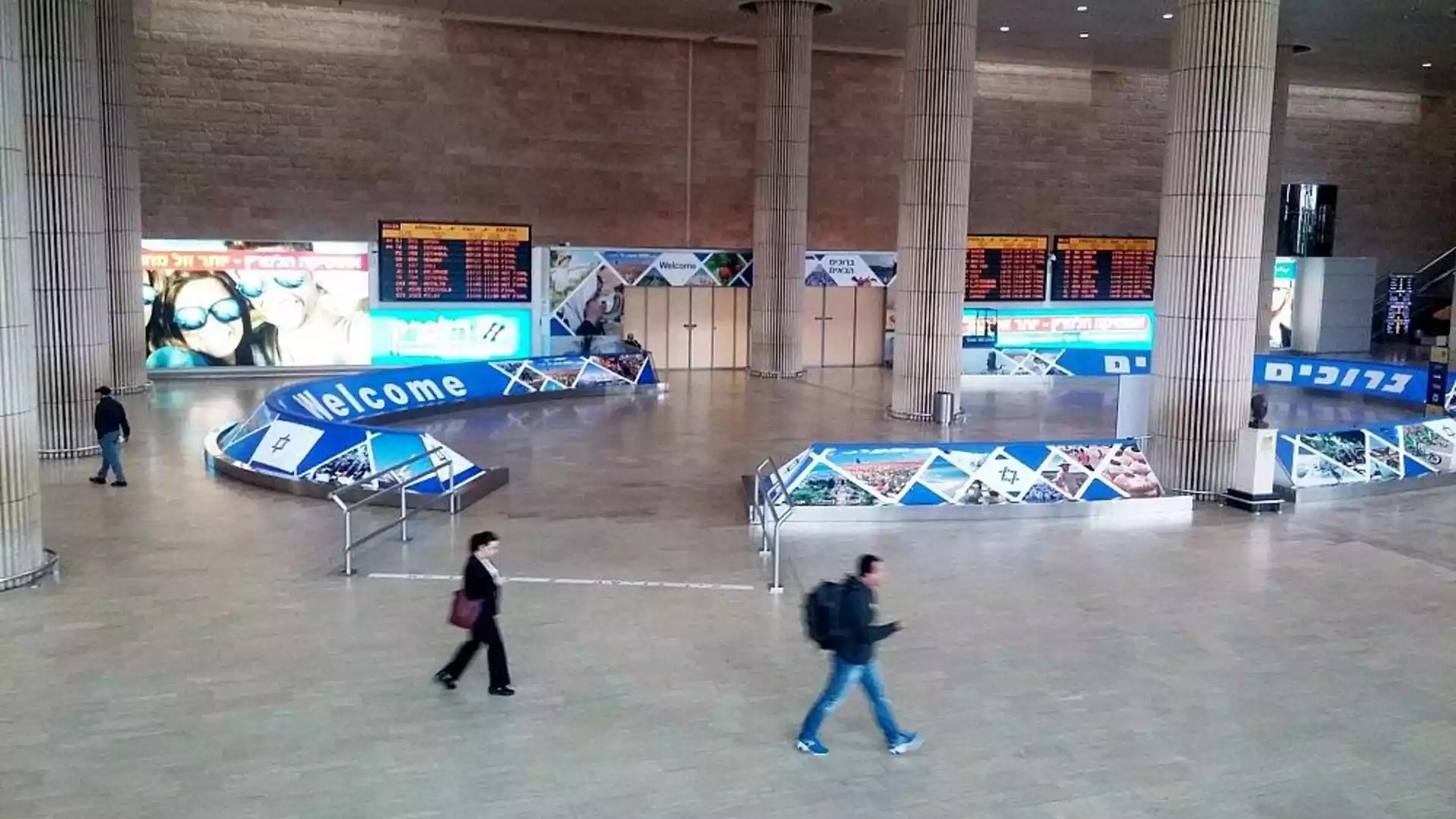 Innenhalle eines Flughafens mit Anzeigetafeln, Begrüßungsbeschilderung und wenigen Passanten.
