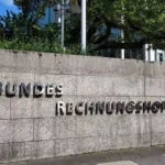 Schild mit dem Schriftzug „Bundesrechnungshof“ an einer Steinmauer vor einem Verwaltungsgebäude.