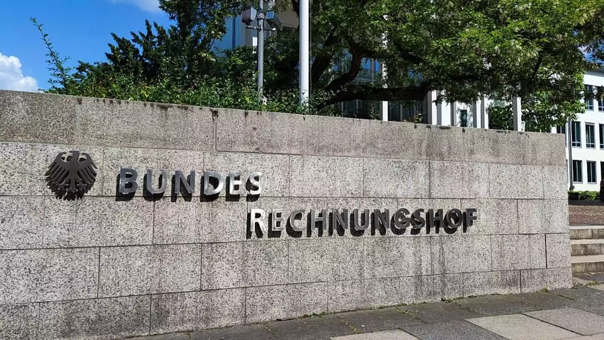 Schild mit dem Schriftzug „Bundesrechnungshof“ an einer Steinmauer vor einem Verwaltungsgebäude.
