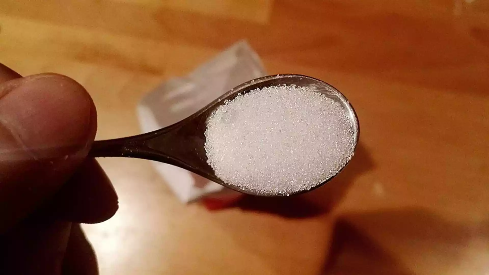Nahaufnahme eines Löffels mit Zuckerkrümeln in einer Hand.