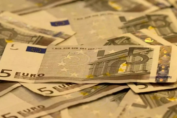 Fünf-Euro-Scheine liegen gestapelt und verstreut auf einer Fläche.