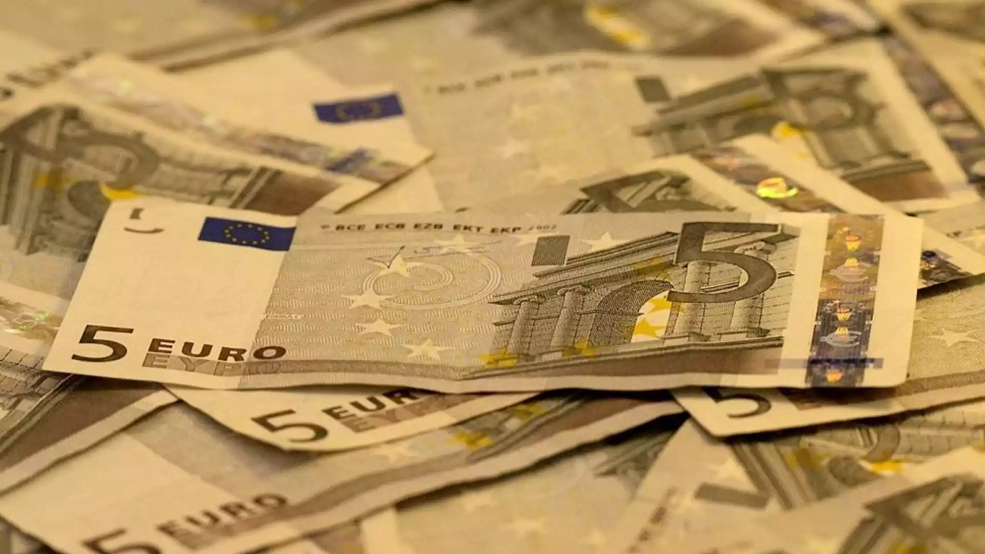 Fünf-Euro-Scheine liegen gestapelt und verstreut auf einer Fläche.