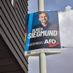 AfD-Wahlplakat mit dem Porträt von Ulrich Siegmund an einem Mast neben einem Gebäude.