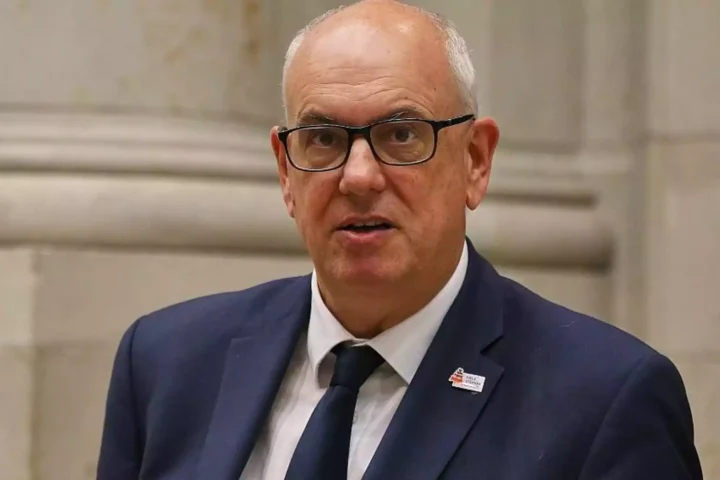 Ein älterer Mann mit Brille und dunklem Anzug spricht vor hellem Hintergrund.
