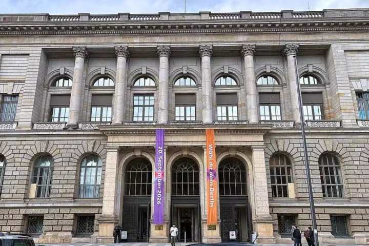 Fassade eines historischen Gebäudes mit Säulen und Bannern vor dem Eingang.
