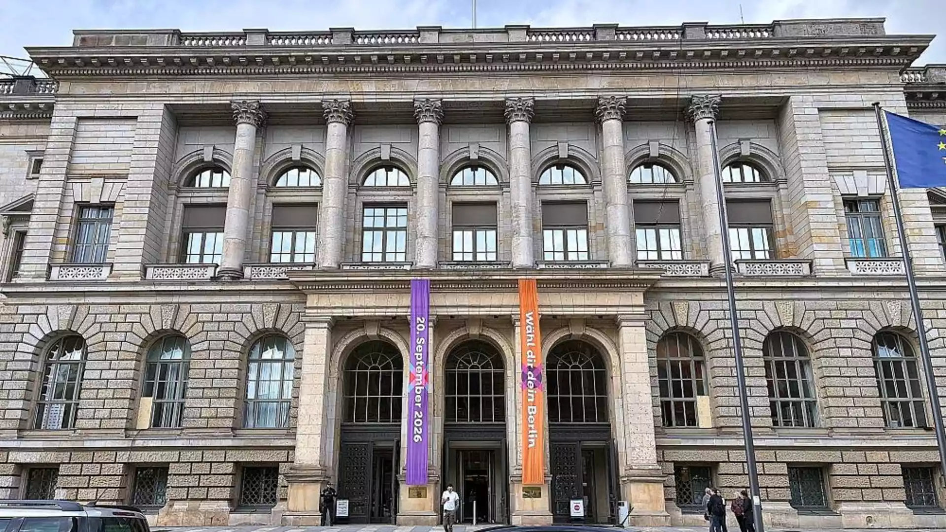 Fassade eines historischen Gebäudes mit Säulen und Bannern vor dem Eingang.