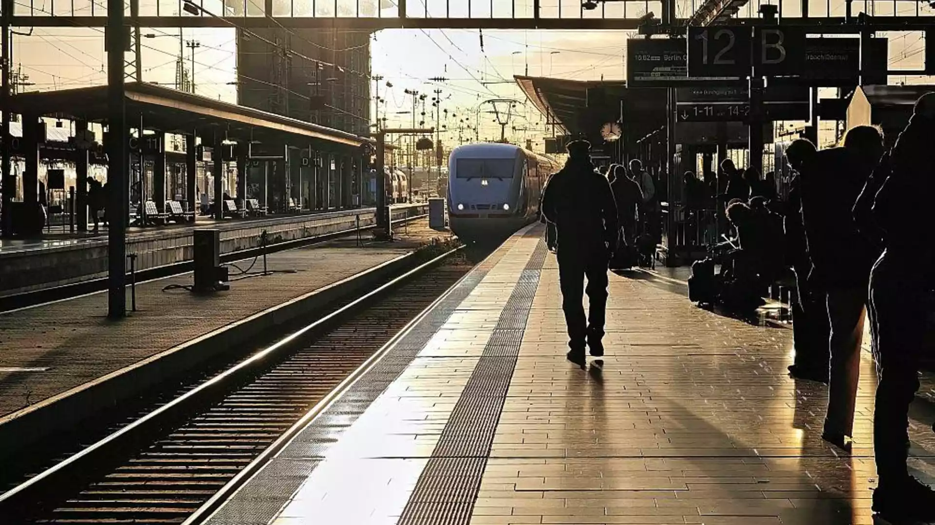Bilger stellt 70-Prozent-Ziel für die Pünktlichkeit der Bahn bis 2029 in Aussicht 1 Ein Zug fährt bei tief stehender Sonne in einen Bahnhof ein, auf dem Bahnsteig warten Reisende im Gegenlicht.