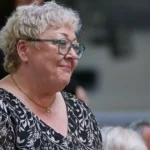 Ältere Frau mit Brille und kurz blondem Haar im Profil.