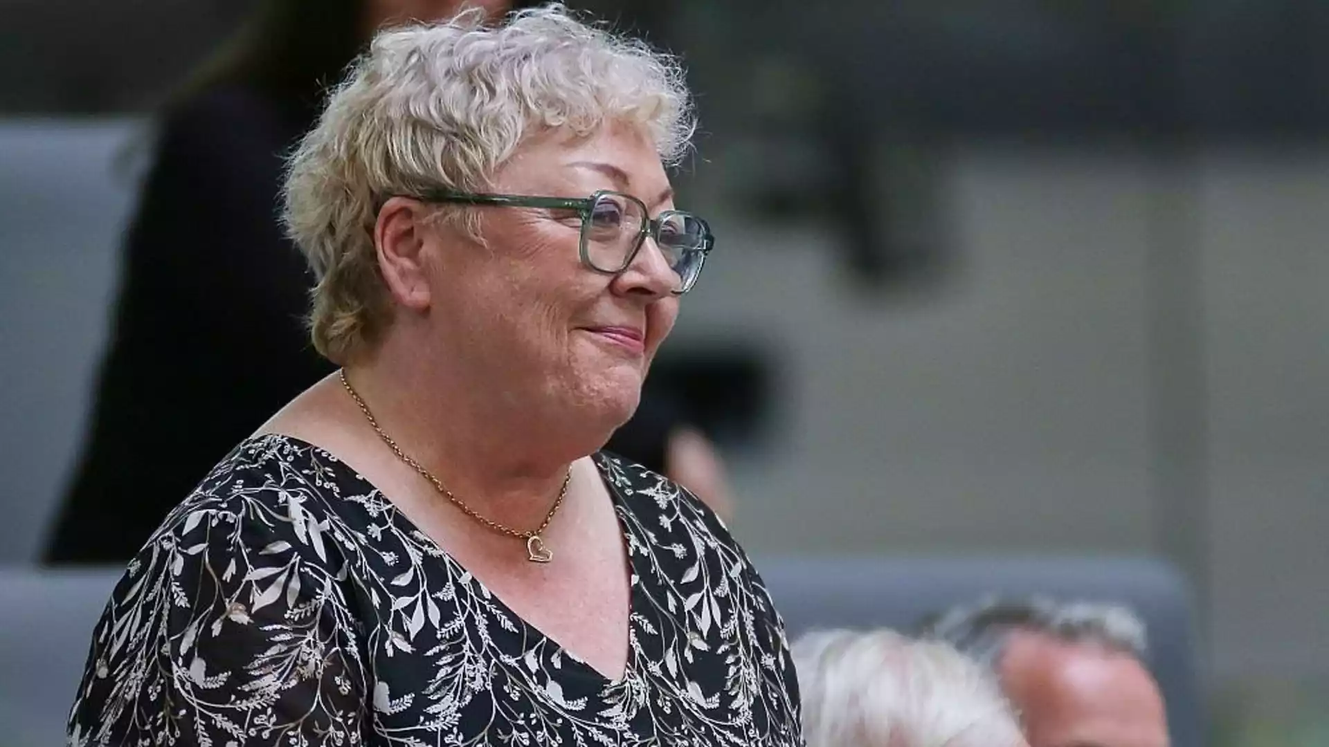 Ältere Frau mit Brille und kurz blondem Haar im Profil.