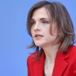 Porträt einer Frau mit rotem Blazer vor blauem Hintergrund.
