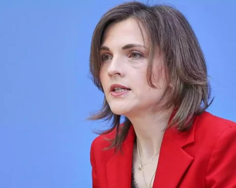 Porträt einer Frau mit rotem Blazer vor blauem Hintergrund.