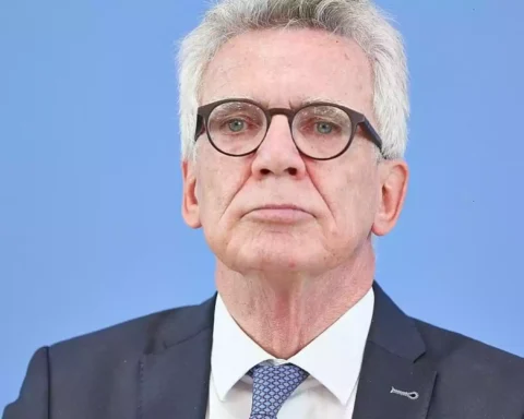 Porträt eines älteren Mannes mit Brille und grauen Haaren im Anzug vor blauem Hintergrund.