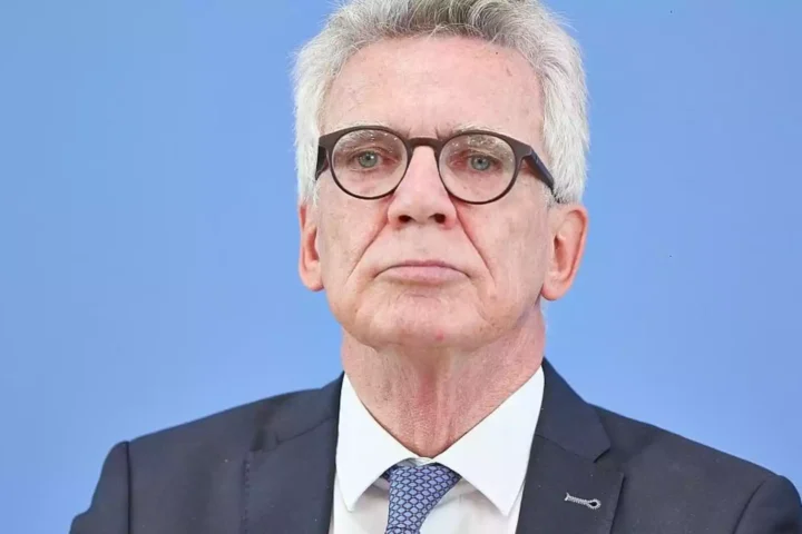 Porträt eines älteren Mannes mit Brille und grauen Haaren im Anzug vor blauem Hintergrund.