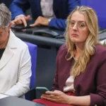 Zwei Politikerinnen sitzen in einer Sitzungsbank im Parlament, eine schaut auf ihr Smartphone.