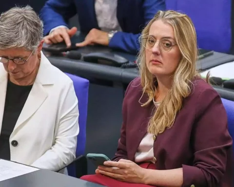 Zwei Politikerinnen sitzen in einer Sitzungsbank im Parlament, eine schaut auf ihr Smartphone.