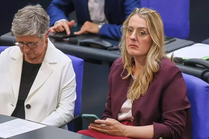 Zwei Politikerinnen sitzen in einer Sitzungsbank im Parlament, eine schaut auf ihr Smartphone.
