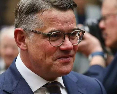 Porträt eines Mannes mit Brille im Anzug in einem politischen Umfeld.