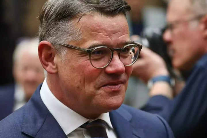 Porträt eines Mannes mit Brille im Anzug in einem politischen Umfeld.
