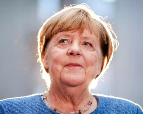 Angela Merkel im Porträt vor grauem Hintergrund mit hellem Gegenlicht.