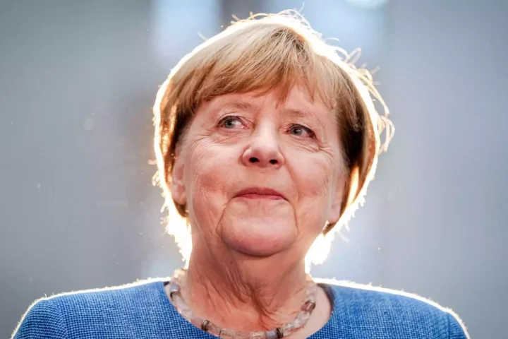 Angela Merkel im Porträt vor grauem Hintergrund mit hellem Gegenlicht.