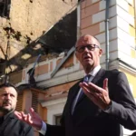 Friedrich Merz spricht vor einem beschädigten Gebäude in Kiew, neben ihm steht Wolodymyr Selenskyj.