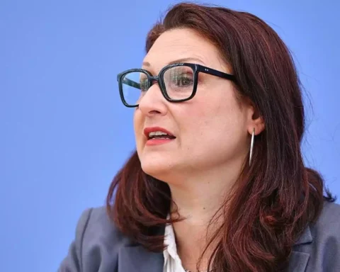 Porträt einer Frau mit Brille vor blauem Hintergrund.
