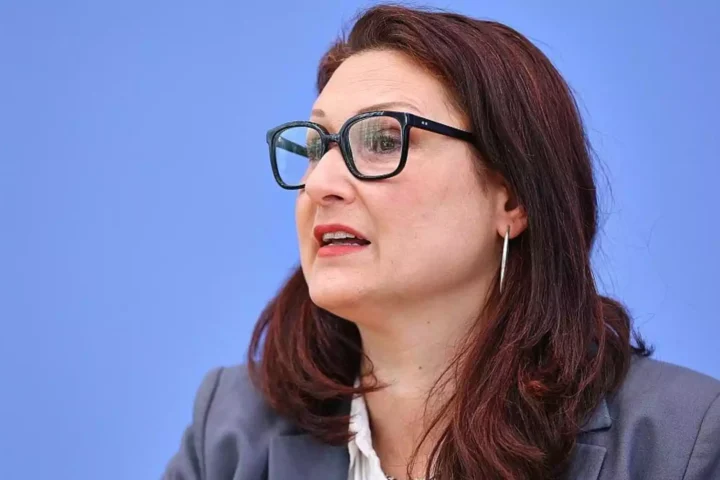 Porträt einer Frau mit Brille vor blauem Hintergrund.