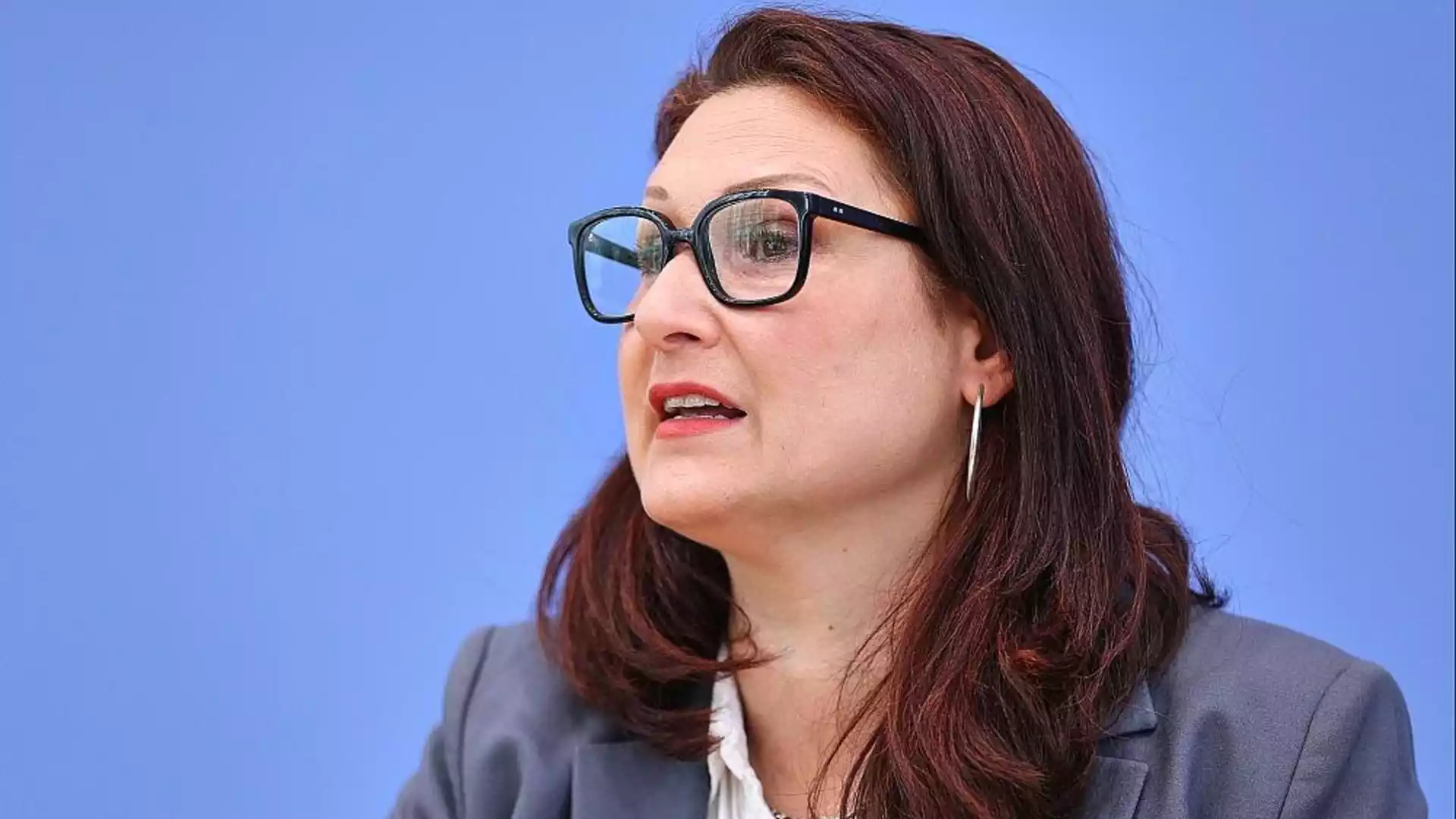 Porträt einer Frau mit Brille vor blauem Hintergrund.