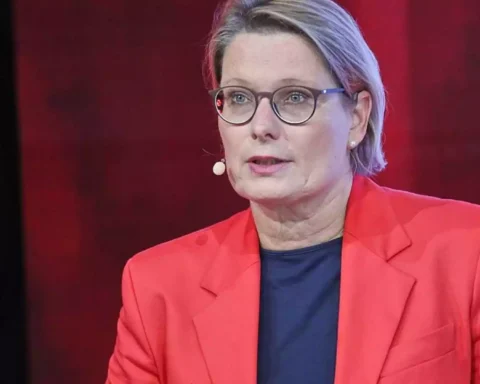 Eine Frau mit Brille und rotem Blazer spricht in einem Fernsehstudio.