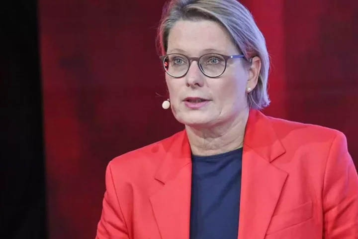 Eine Frau mit Brille und rotem Blazer spricht in einem Fernsehstudio.