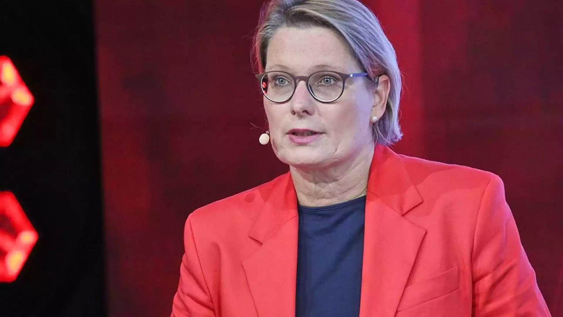 Eine Frau mit Brille und rotem Blazer spricht in einem Fernsehstudio.