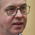 Nahaufnahme eines Mannes mit Brille vor hellem Hintergrund.