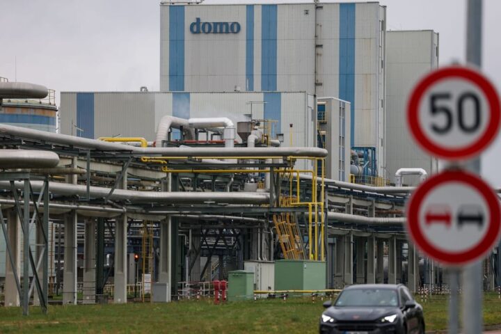Industrieanlage mit Rohrleitungen und Gebäude mit der Aufschrift „domo“, davor Verkehrsschilder und ein Auto.