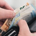Hände ziehen Euro-Banknoten aus einer schwarzen Geldbörse.