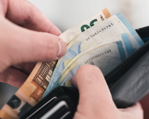 Hände ziehen Euro-Banknoten aus einer schwarzen Geldbörse.