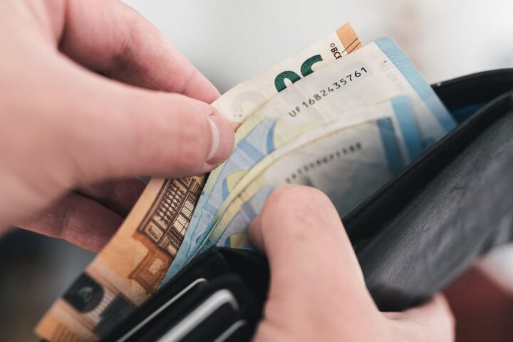 Hände ziehen Euro-Banknoten aus einer schwarzen Geldbörse.