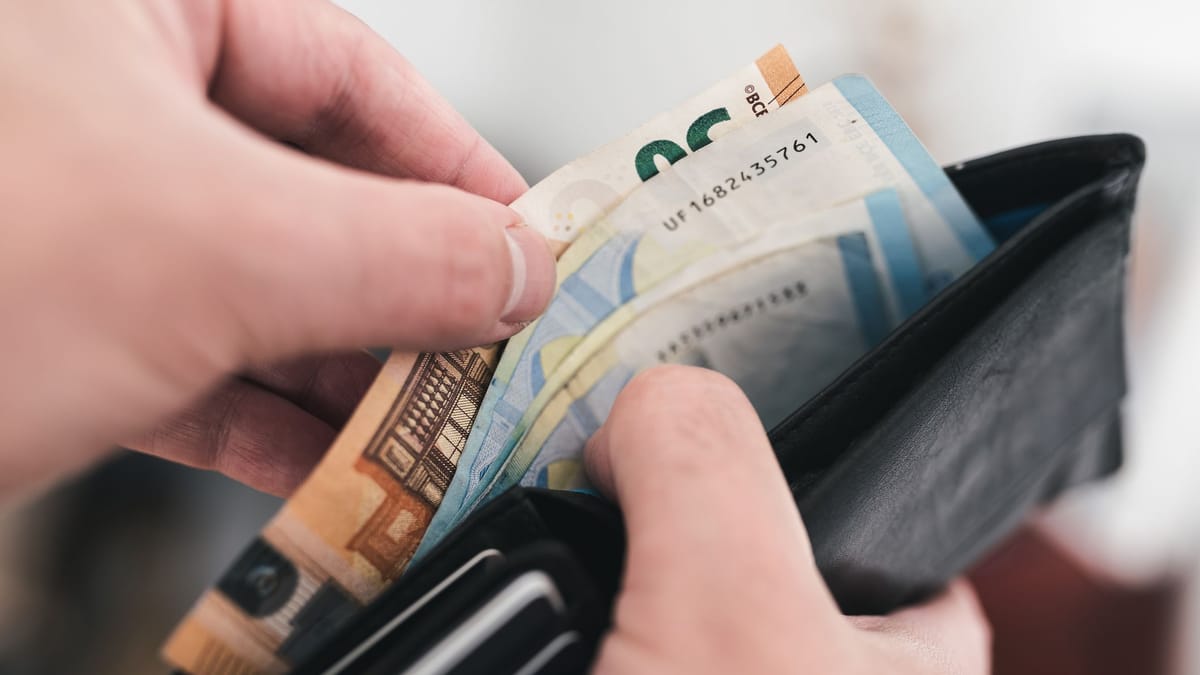 Hände ziehen Euro-Banknoten aus einer schwarzen Geldbörse.