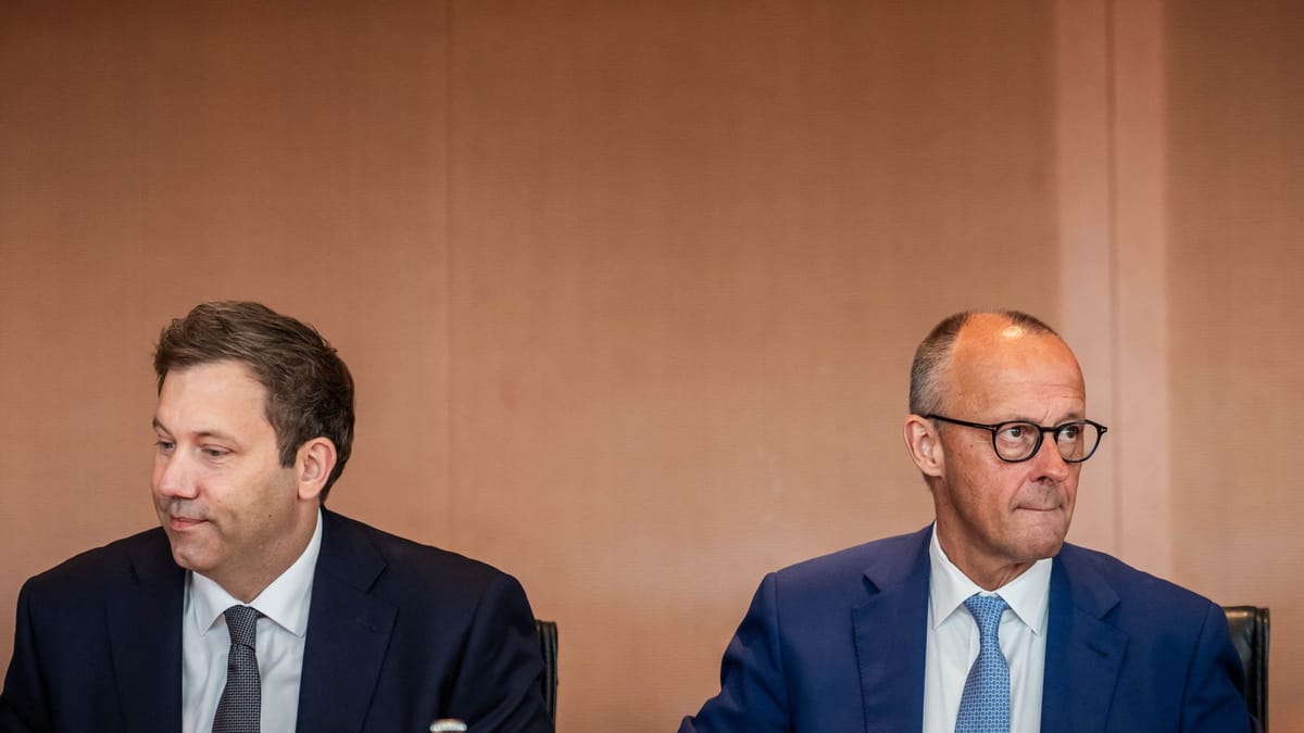 Zwei Männer im Anzug sitzen bei einem Treffen nebeneinander.