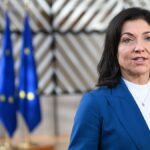 Katherina Reiche vor mehreren EU-Flaggen in einem Innenraum.